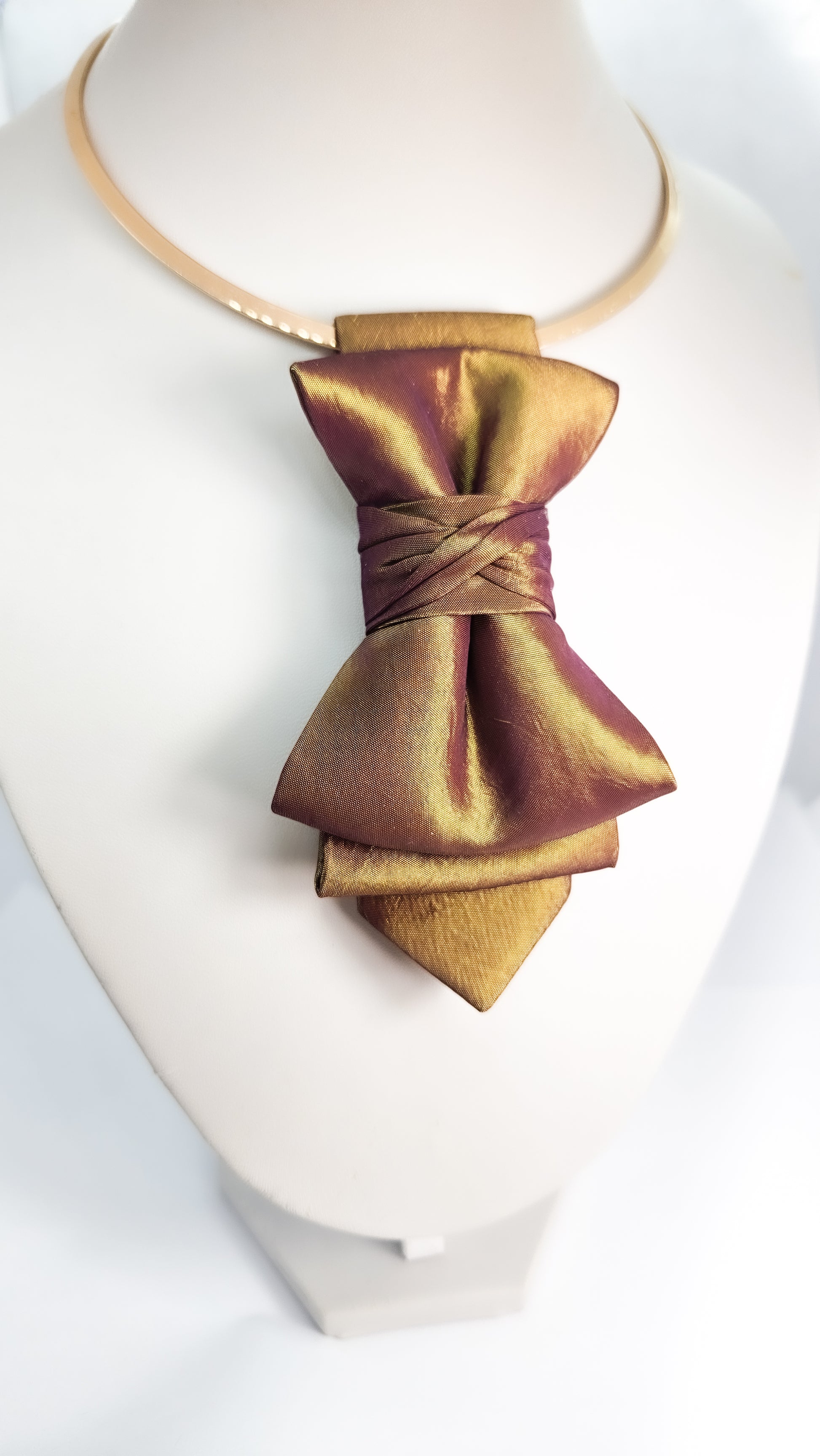 Gold bow tie on a mannequin head with a white background metallic plum gold womens necktie, bronze burgundy metallic bow tie for women, chameleon fabric neck accessory, handmade statement necktie, sculptural womens neckwear, metallic plum bronze neckpiece, luxury handmade womens neck accessory, artistic fabric necktie, modern designer womens bow tie, elegant metallic neckwear, unique womens fashion necktie, gold burgundy neck accessory, contemporary statement neckpiece