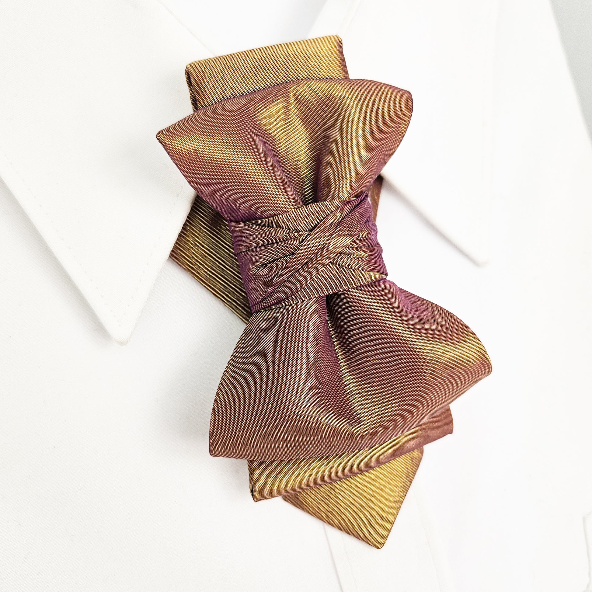 Folded fabric with a decorative bow on a white background metallic plum gold womens necktie, bronze burgundy metallic bow tie for women, chameleon fabric neck accessory, handmade statement necktie, sculptural womens neckwear, metallic plum bronze neckpiece, luxury handmade womens neck accessory, artistic fabric necktie, modern designer womens bow tie, elegant metallic neckwear, unique womens fashion necktie, gold burgundy neck accessory, contemporary statement neckpiece