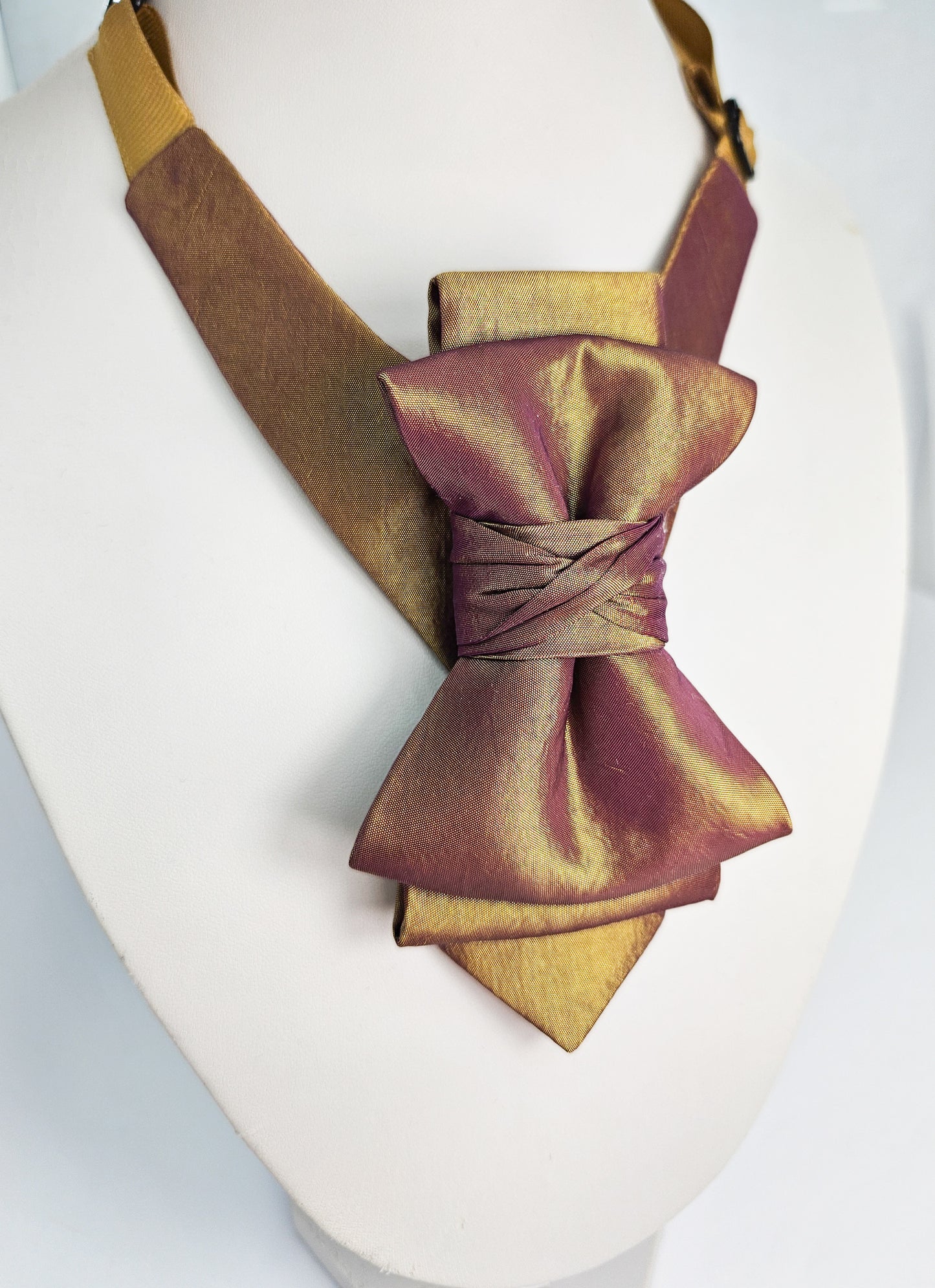 Gold and brown bow tie on a mannequin with a white background metallic plum gold womens necktie, bronze burgundy metallic bow tie for women, chameleon fabric neck accessory, handmade statement necktie, sculptural womens neckwear, metallic plum bronze neckpiece, luxury handmade womens neck accessory, artistic fabric necktie, modern designer womens bow tie, elegant metallic neckwear, unique womens fashion necktie, gold burgundy neck accessory, contemporary statement neckpiece
