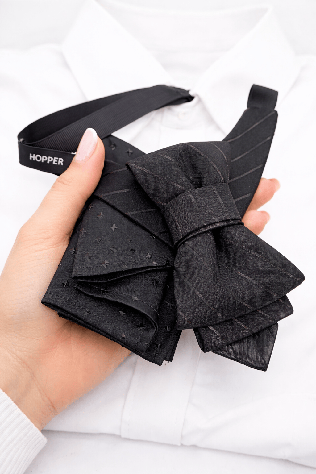 Black bow tie held by a hand on a white background handmade black bow tie for men, black wedding bow tie for groom, unique black statement bow tie, luxury handmade black bow tie, designer black bow tie men, modern black wedding bow tie, artistic black bow tie design, groom statement bow tie black, black formal bow tie unisex, alternative black bow tie style, creative handmade black neckwear, stylish black bow tie events, elegant modern black bow tie, fashion forward black bow tie, bold designer black bow ti