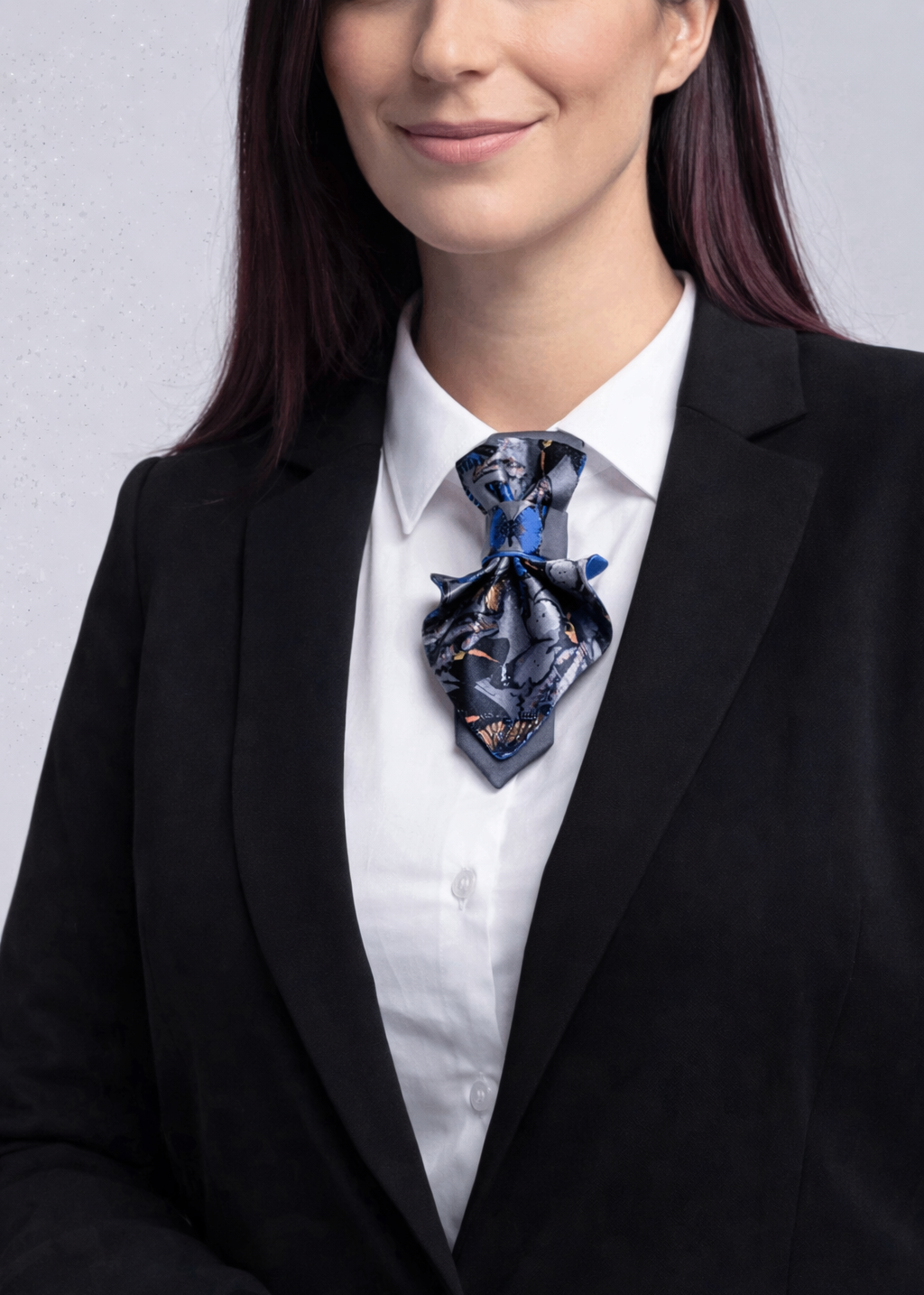 Person wearing a black suit with a patterned tie against a plain background