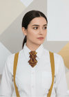 Woman wearing a white shirt with a decorative brooch and suspenders against a geometric background metallic plum gold womens necktie, bronze burgundy metallic bow tie for women, chameleon fabric neck accessory, handmade statement necktie, sculptural womens neckwear, metallic plum bronze neckpiece, luxury handmade womens neck accessory, artistic fabric necktie, modern designer womens bow tie, elegant metallic neckwear, unique womens fashion necktie, gold burgundy neck accessory, contemporary statement neckpi