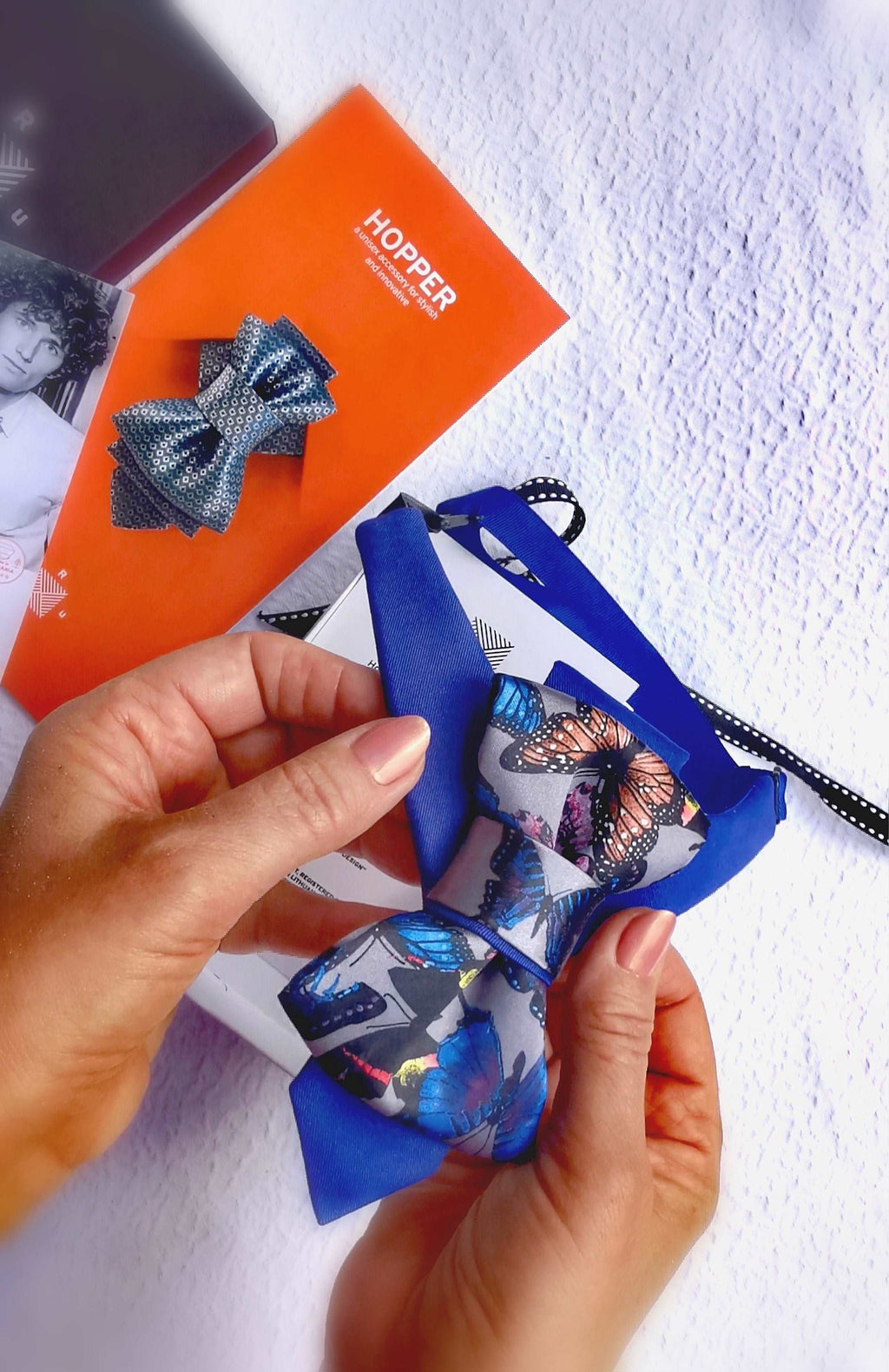 HOPPER TIE BUTTERFLYHandmade blue bow tie with butterfly print, Pre-tied bow tie for special occasions, Elegant unisex accessory with colorful butterflies, Blue bow tie with vibrant butterfly pattern, Luxury butterfly bow tie in gift box, Family-friendly handmade tie from Lithuania, Stylish blue bow tie for all ages, Fashion bow tie designed by Rūta Piekurienė