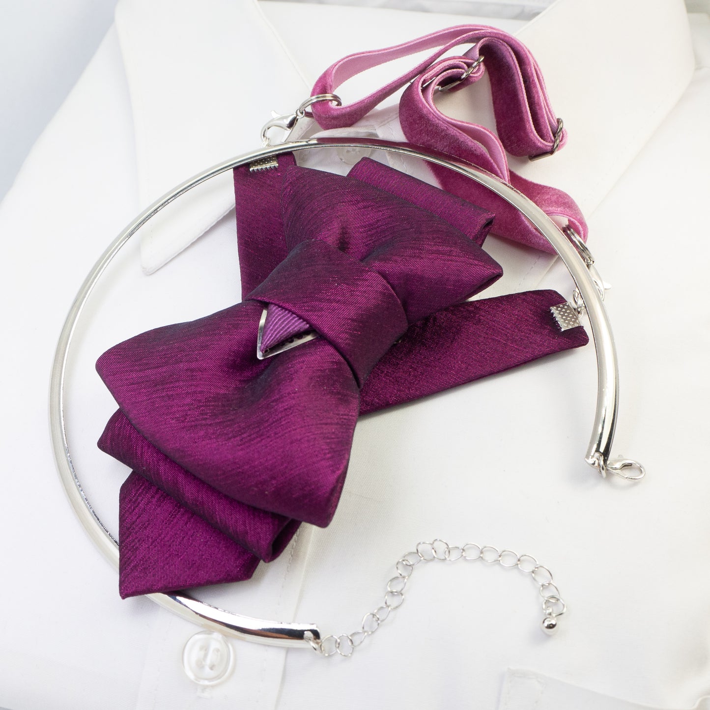 A pre-tied fabric bow tie in shades of pink and purple, displayed on a white shirt collar.