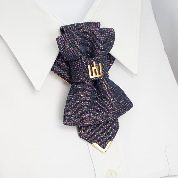 Navy blue textured bow tie with gold accents on a white background Exclusive handmade jabot necktie in shimmering black with gold and purple details, accented with Gediminas Pillars symbol. Luxury wedding tie for groom or guest, perfect accessory for cultural gatherings, ceremonies, and elegant evening wear. Unique artisan craftsmanship, high-quality Lithuanian design. Artisan handmade tie in jabot silhouette, crafted from dark shimmering fabric with purple-gold texture and golden Gediminas Columns accent. 