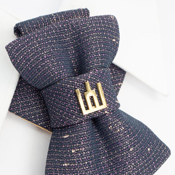 Folded navy blue textured fabric with a gold brooch on a white background Exclusive handmade jabot necktie in shimmering black with gold and purple details, accented with Gediminas Pillars symbol. Luxury wedding tie for groom or guest, perfect accessory for cultural gatherings, ceremonies, and elegant evening wear. Unique artisan craftsmanship, high-quality Lithuanian design.