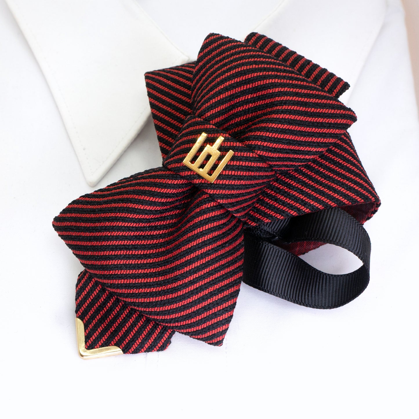 Red and black striped bow tie with gold emblem on a white background red black striped jabot tie, gold Gedimino stulpai emblem, handmade heritage necktie, Lithuanian cultural fashion, artisan jabot-style tie, elegant striped tie gold badge, luxury heritage necktie, cultural fashion accessory, Lithuanian identity tie, formal jabot tie, handcrafted Lithuanian motif tie