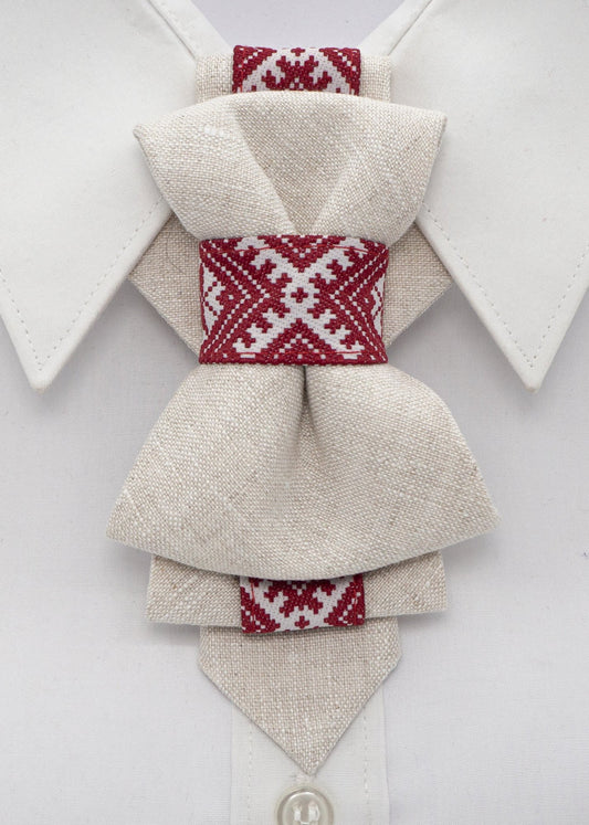 A beige linen vertical bow tie with red ethnic motifs, displayed on a white shirt collar.