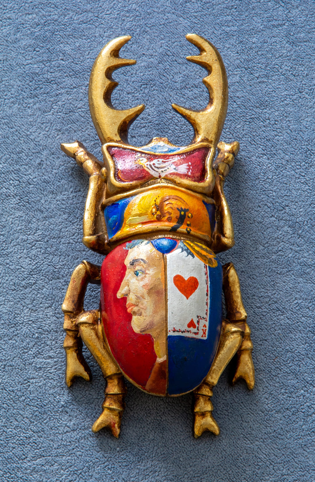 Decorative beetle-shaped object with gold antlers and colorful face on a blue background