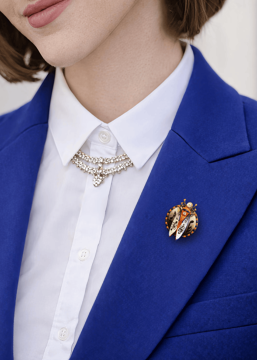 Person wearing a blue blazer with a white shirt and decorative brooch hand painted insect brooch, enamel beetle brooch, cicada brooch jewelry, rhinestone insect brooch, colorful bug brooch, artistic insect pin, handmade enamel brooch, statement insect jewelry, unique bug brooch, designer insect brooch, red black white beetle brooch, decorative insect pin, nature inspired brooch, collectible insect jewelry, whimsical bug brooch, vintage style insect brooch, artistic enamel insect pin, crystal insect brooch, 