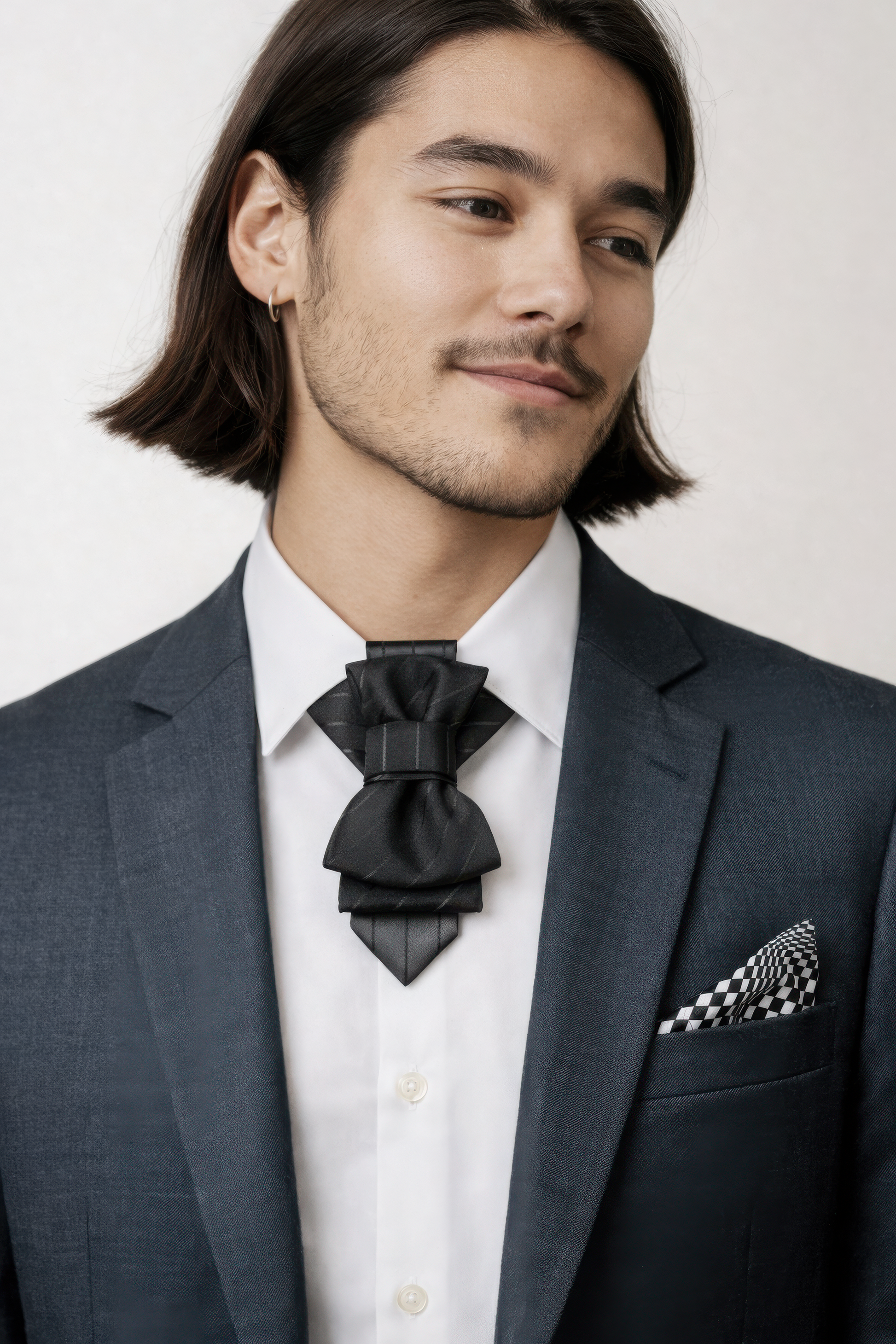 Man wearing a dark suit with a black bow tie and checkered pocket square on a white background handmade black bow tie for men, black wedding bow tie for groom, unique black statement bow tie, luxury handmade black bow tie, designer black bow tie men, modern black wedding bow tie, artistic black bow tie design, groom statement bow tie black, black formal bow tie unisex, alternative black bow tie style, creative handmade black neckwear, stylish black bow tie events, elegant modern black bow tie, fashion forwa