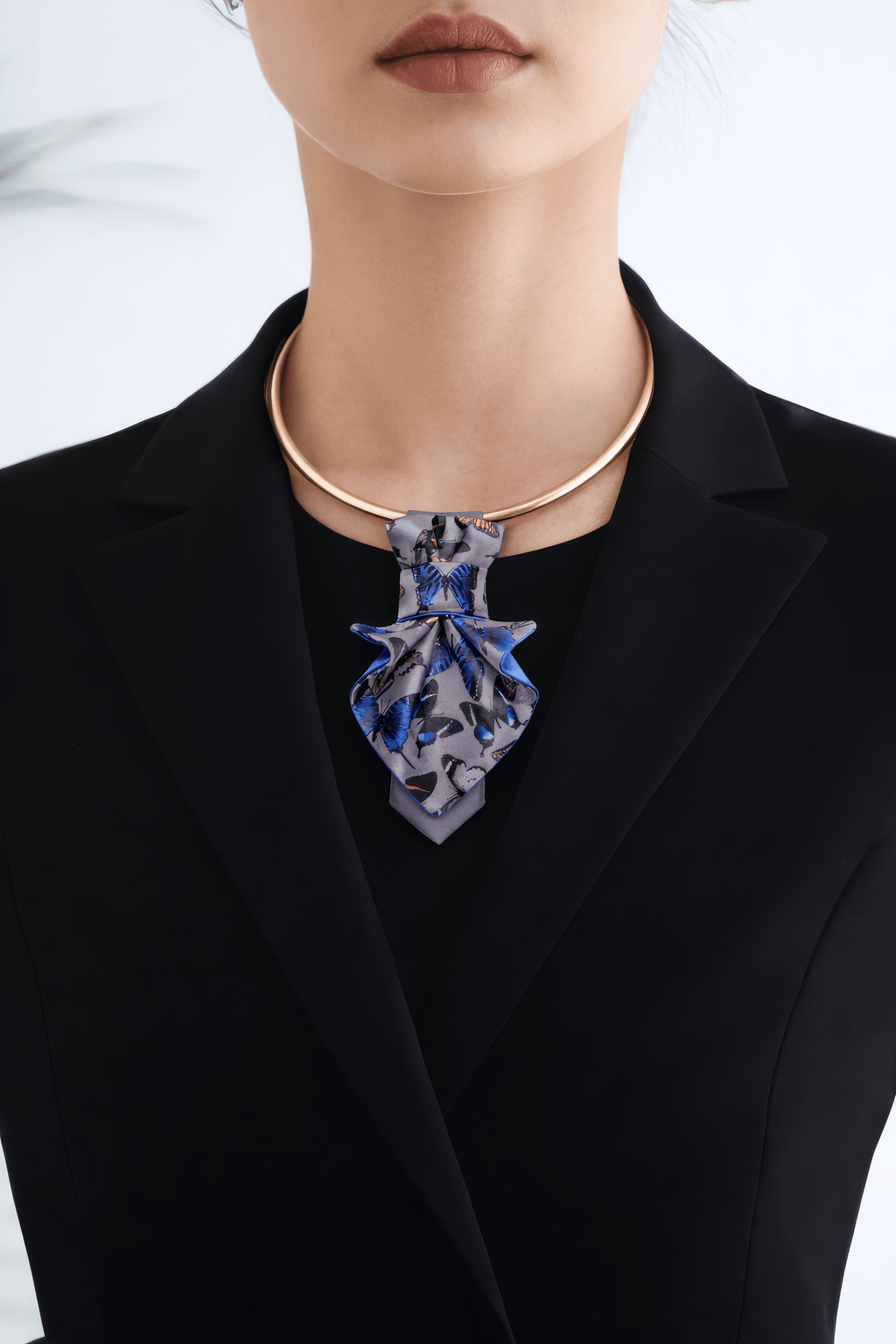 Person wearing a black blazer with a blue floral necklace against a white background Person wearing a black blazer with a patterned tie against a blurred indoor background Jabot Blue tie for women, Blue bow tie for ladies Handmade luxury women’s necktie “Butterfly” – elegant gray and blue accessory with butterfly pattern, combining tie and bow style, perfect for weddings, musicians, and artistic women.