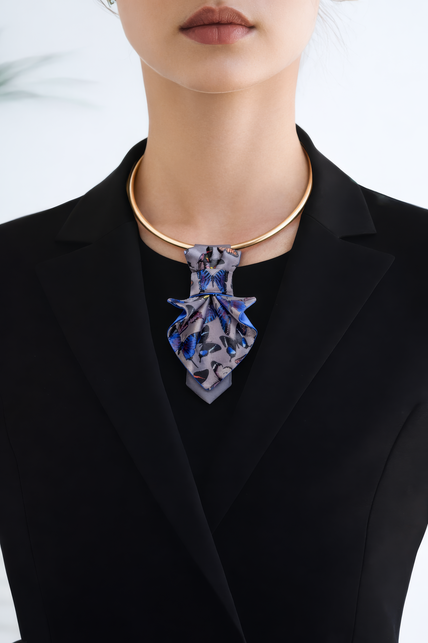 Person wearing a black blazer with a blue floral necklace against a white background Person wearing a black blazer with a patterned tie against a blurred indoor background Jabot Blue tie for women, Blue bow tie for ladies Handmade luxury women’s necktie “Butterfly” – elegant gray and blue accessory with butterfly pattern, combining tie and bow style, perfect for weddings, musicians, and artistic women.