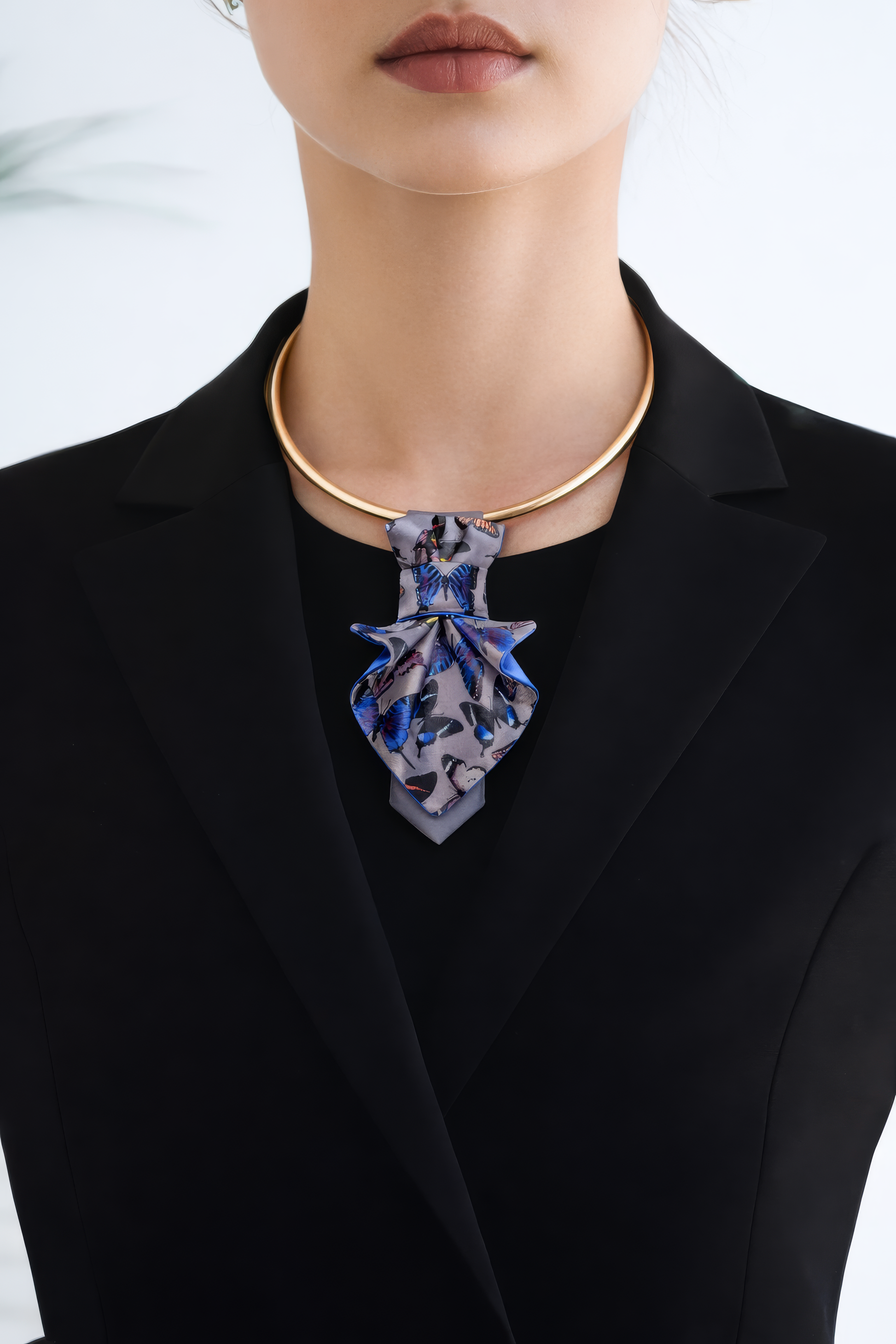 Person wearing a black blazer with a blue floral necklace against a white background Person wearing a black blazer with a patterned tie against a blurred indoor background Jabot Blue tie for women, Blue bow tie for ladies Handmade luxury women’s necktie “Butterfly” – elegant gray and blue accessory with butterfly pattern, combining tie and bow style, perfect for weddings, musicians, and artistic women.