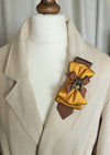 Gold bumblebee brooch and mustard yellow bow tie styled on a beige jacket lapel.