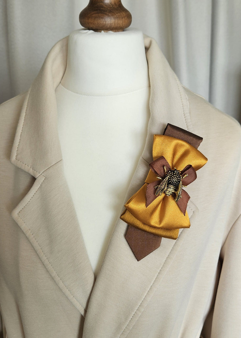 Gold bumblebee brooch and mustard yellow bow tie styled on a beige jacket lapel.