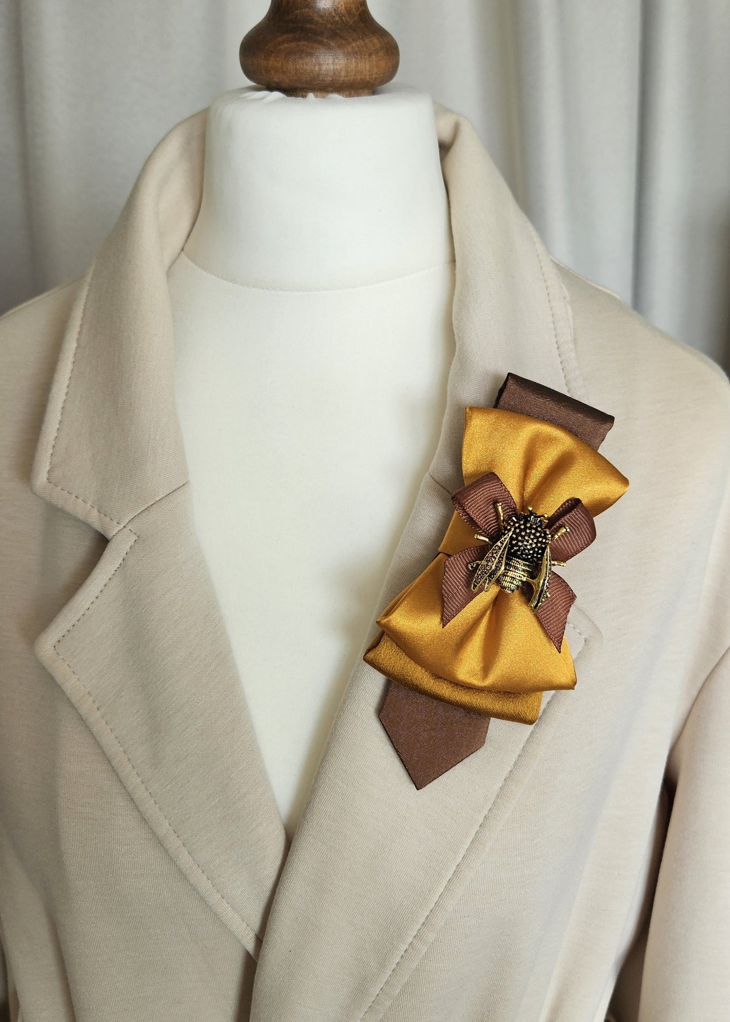Gold bumblebee brooch and mustard yellow bow tie styled on a beige jacket lapel.