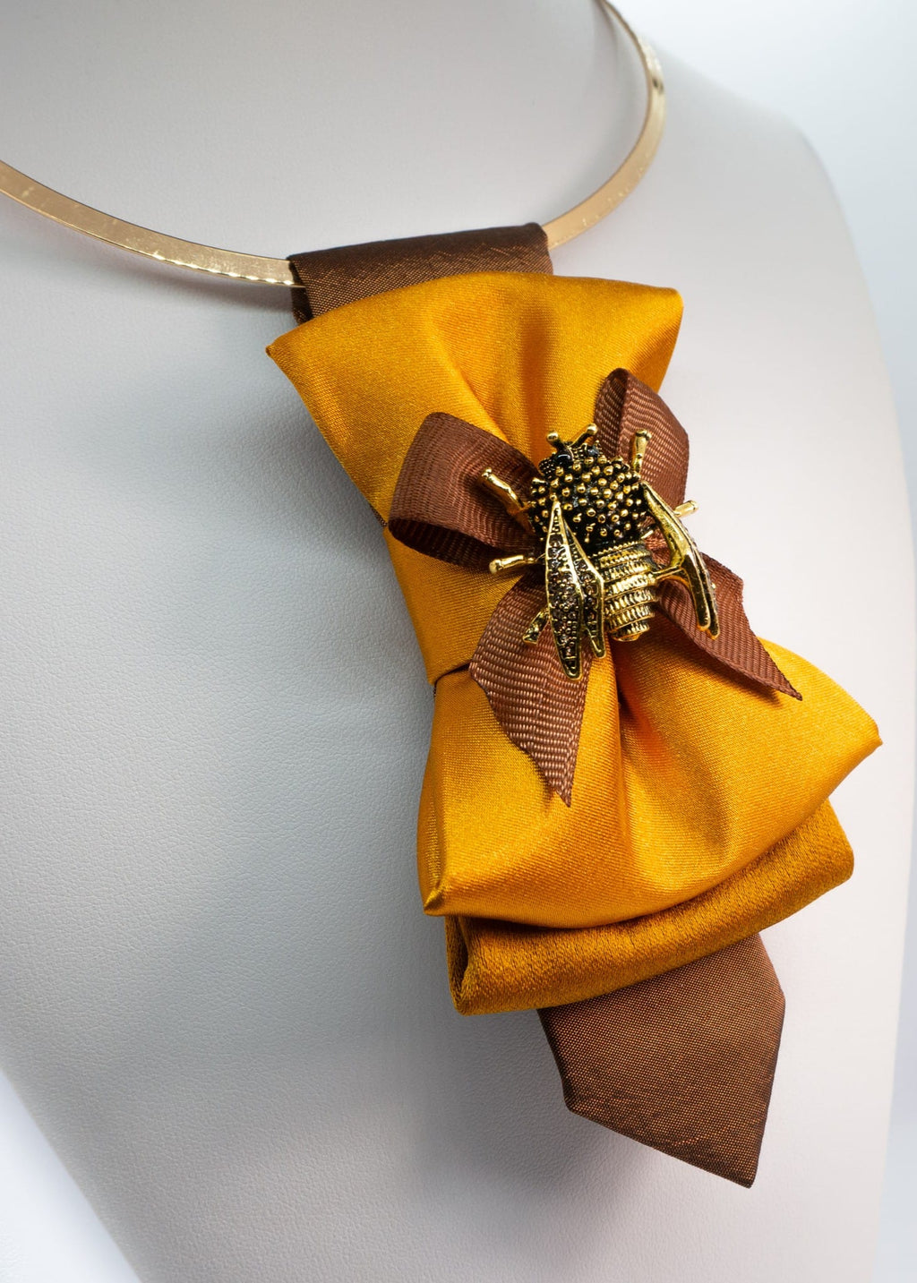 Close-up of the intricate gold bumblebee brooch on a mustard yellow satin tie.
