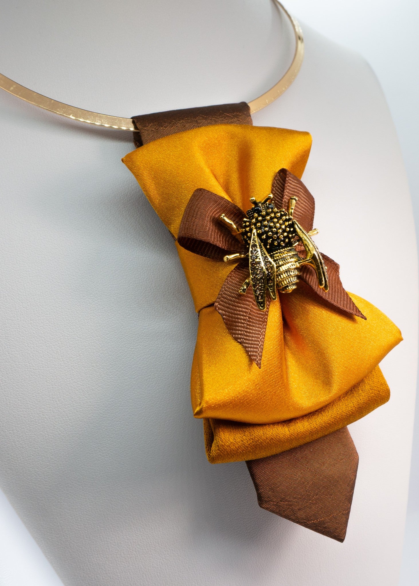 Close-up of the intricate gold bumblebee brooch on a mustard yellow satin tie.