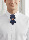 Man wearing a white shirt with a dark blue tie featuring colorful pins, standing in a room with decorative elements. ithuanian heritage necktie, Gediminas Pillars tie, handmade symbolic tie, Baltic cultural accessory, jabot style neckwear, patriotic men’s fashion, tricolor ribbon necktie, freedom identity tie, elegant historical neckwear, Baltic pride tie, artisan men’s tie, traditional symbol cravat, modern ethnic accessory, small nation support fashion, Mediterranean style tie, wedding necktie for groom, 