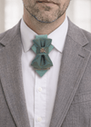 Man wearing a gray suit with a white shirt and a decorative blue bow tie handmade luxury hopper tie, 13 cm vertical bow tie necklace, unique designer neck accessory, teal and gold fabric tie with metal pin, modern unisex statement tie, artistic wedding neckwear, groom alternative tie, minimalist luxury fashion accessory, handcrafted european design neckpiece