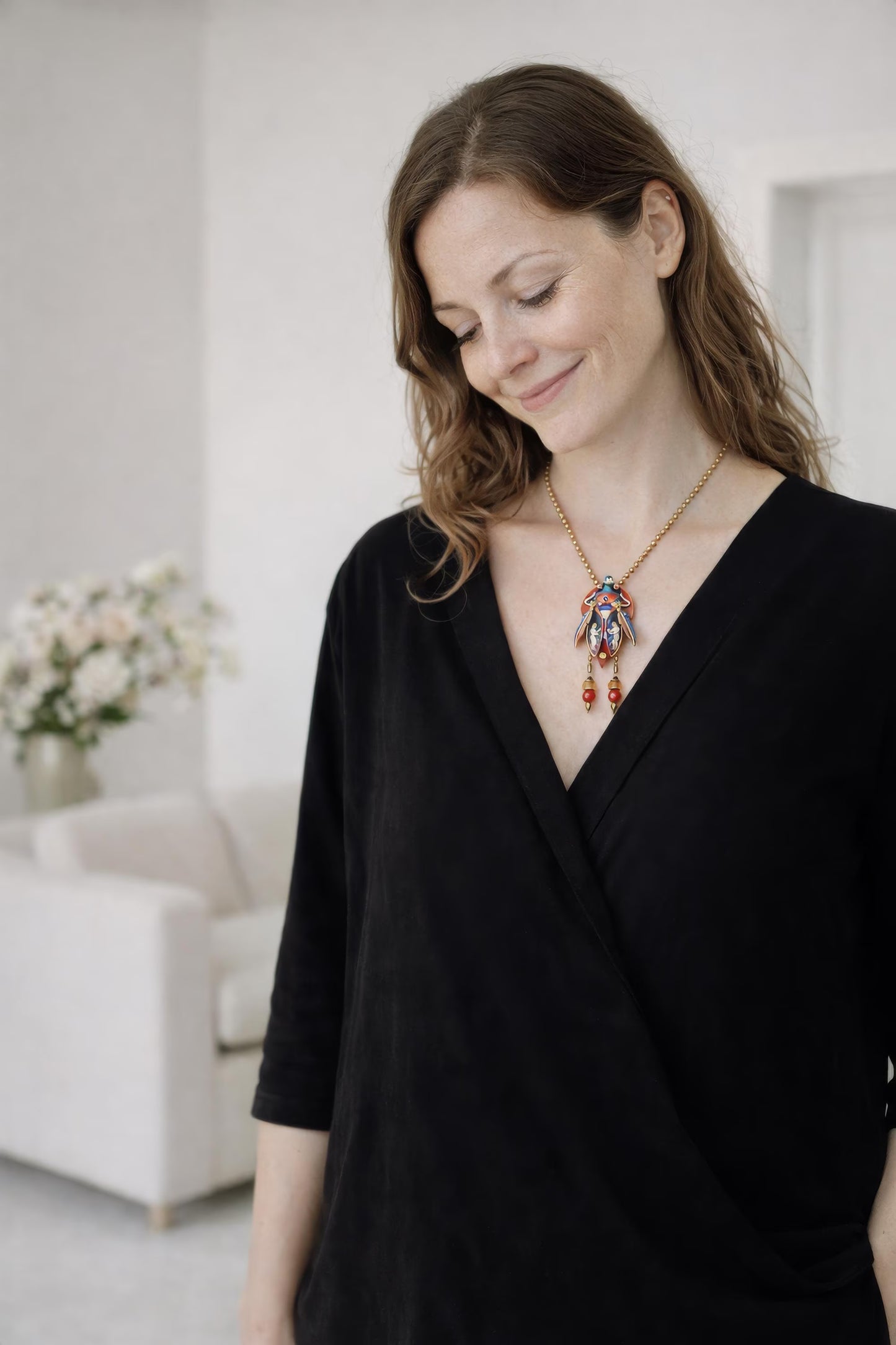 Woman wearing a black top and colorful necklace in a room with white walls and a couch unique gift for her, art lover gift, handmade jewelry gift, collectible art necklace, luxury statement gift, anniversary gift idea, birthday gift for wife, gift for creative woman, meaningful artistic jewelry, museum style pendant gift, renaissance inspired necklace, fantasy insect jewelry, heirloom style accessory, artisan designer necklace, special occasion jewelry, romantic gift idea, Christmas gift for her, Valentine 