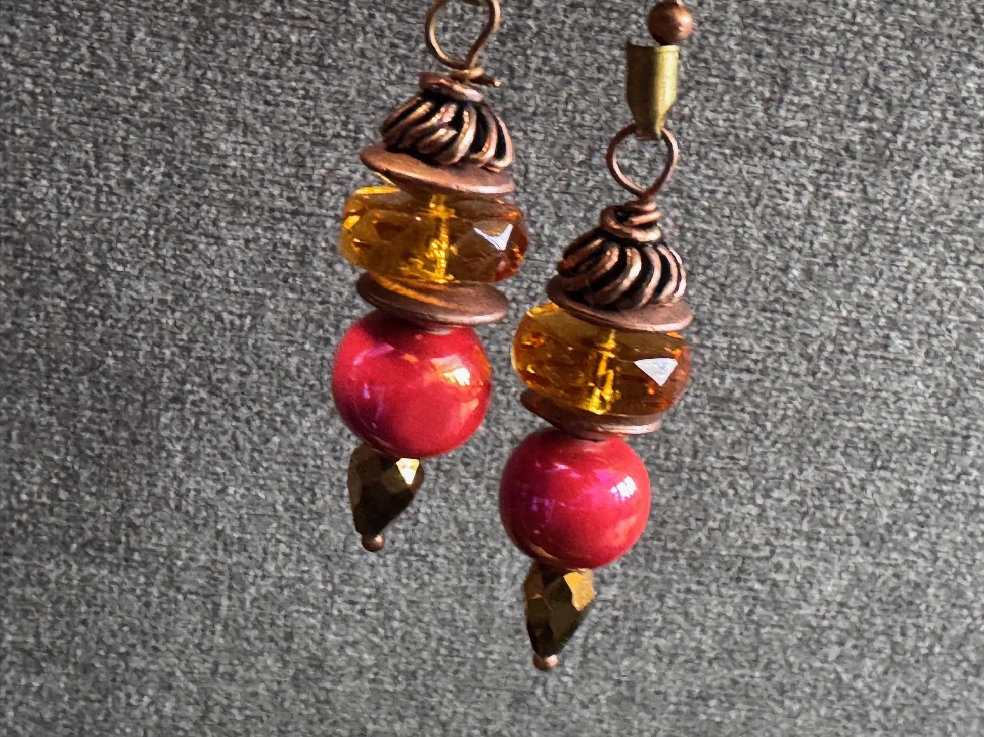 Pair of earrings with red and amber beads on a gray background