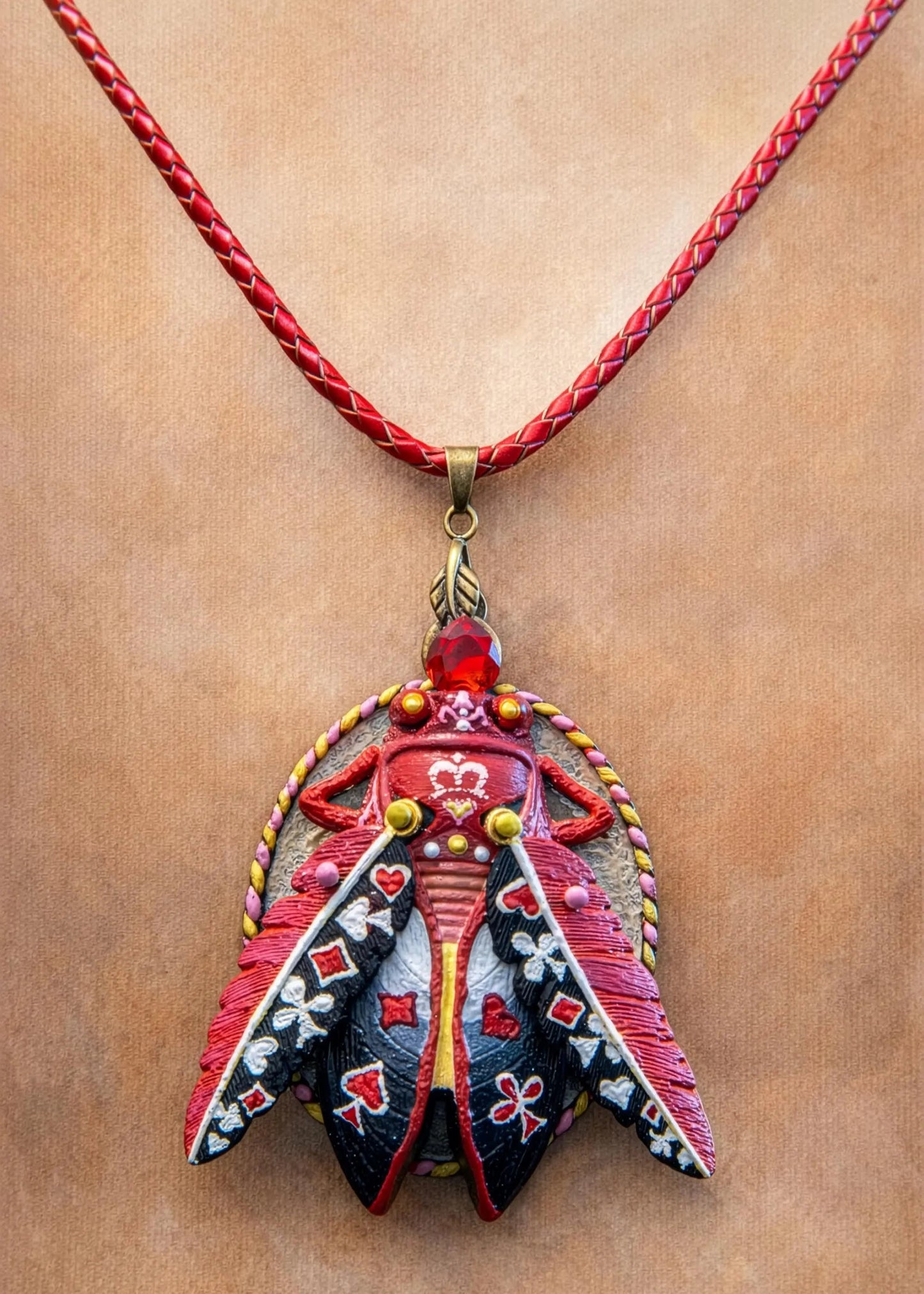 Colorful pendant necklace with intricate design on a red cord against a beige background hand painted scarab necklace red black pendant, statement insect neck accessory, unique artist jewelry for women, bold red cord pendant necklace, wearable art beetle pendant, handmade enamel scarab charm, artistic fashion necklace close up, one of a kind insect jewelry, luxury artisan pendant for art lover, red gemstone scarab necklace, contemporary statement neckpiece, collectible art jewelry pendant, designer handmade
