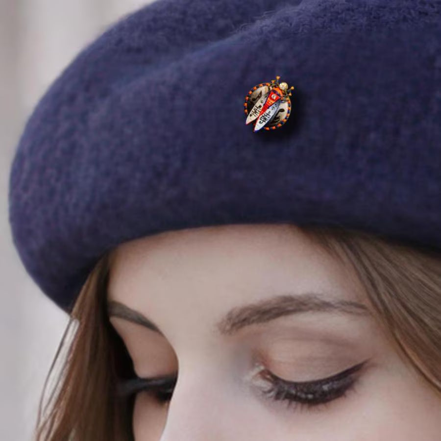Close-up of a person wearing a navy blue beret with a decorative button. Musical scarab brooch with hand painted music notes, unique artist beetle pin white background, handmade luxury music themed brooch, original art jewelry for musician gift, one of a kind painted insect brooch, red blue gold statement accessory, wearable art scarab with notes motif, artistic music lover brooch gift, handcrafted collectible beetle pin, exclusive small batch art jewelry