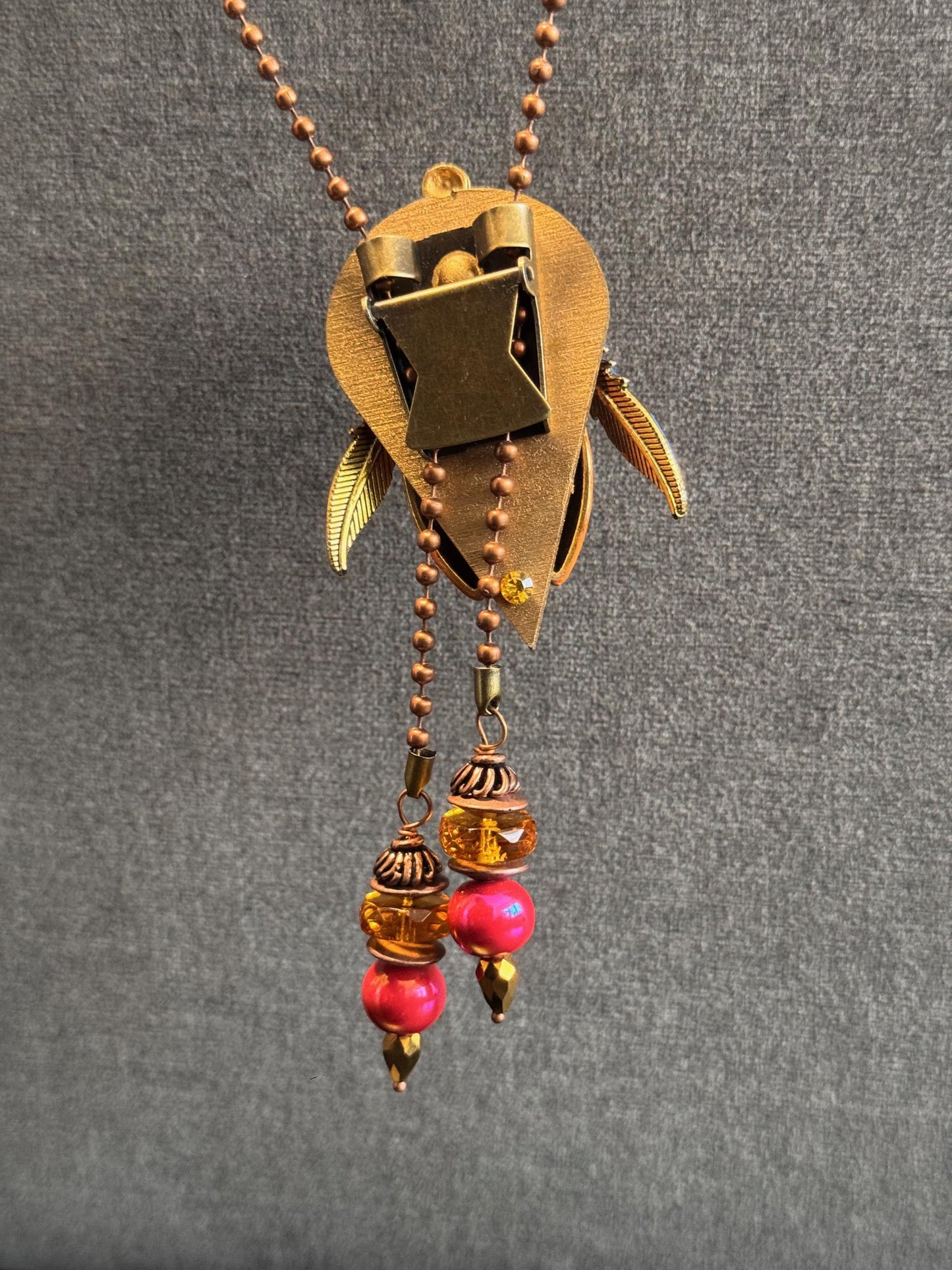 Decorative necklace with gold pendant and red beads on a gray background