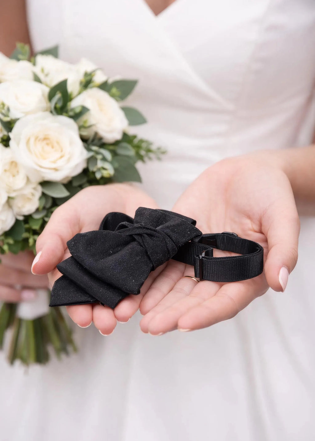 Person holding black ribbons with a bouquet of white flowers in the background