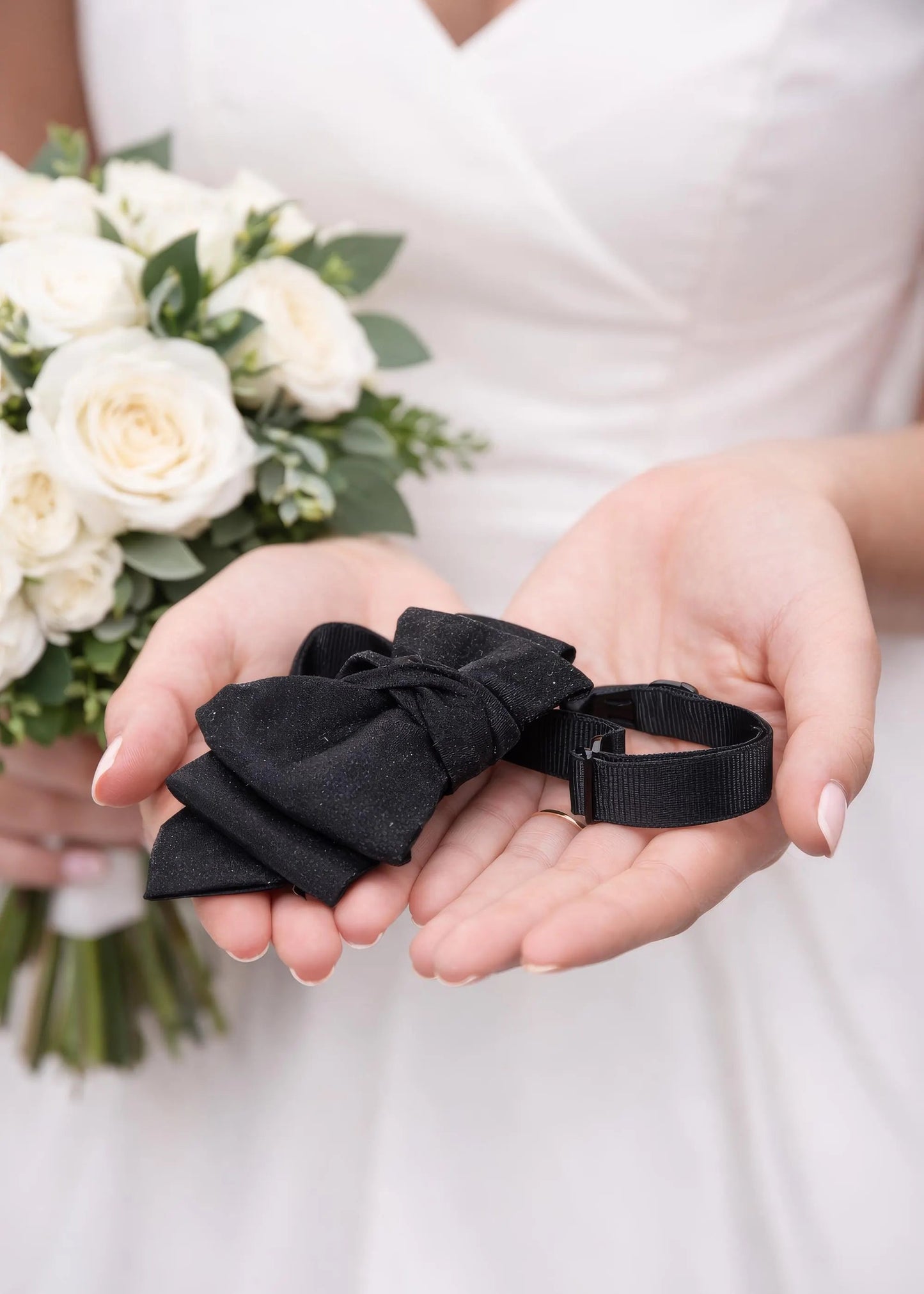 Person holding black ribbons with a bouquet of white flowers in the background