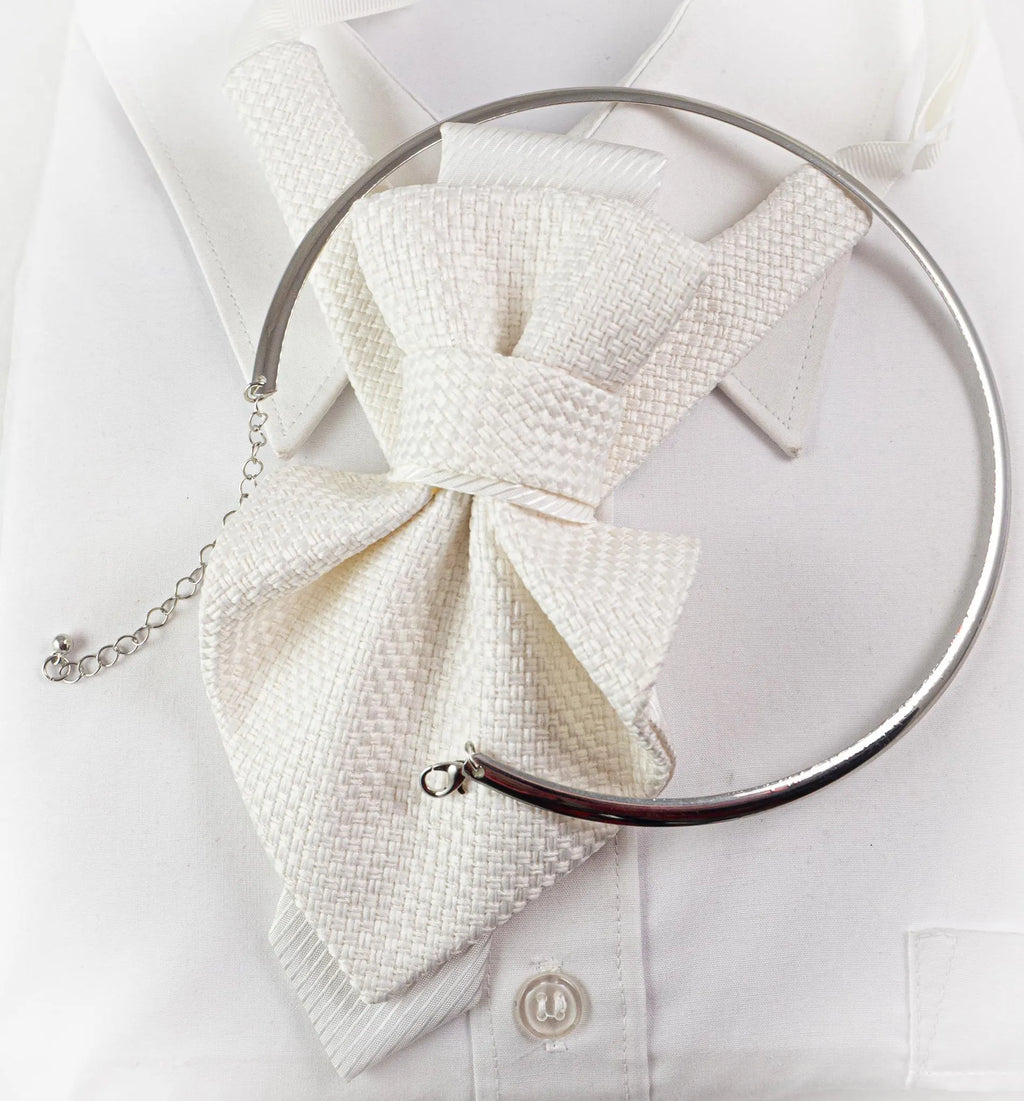 A silver-toned metal neck ring with an attached chain extender, styled on a white textured bow tie and white dress shirt May include: A white textured cravat featuring a woven pattern, layered over a white collared shirt. The cravat is secured by a smooth, silver-toned metal collar necklace that encircles the neck area, complete with a delicate chain and lobster clasp.