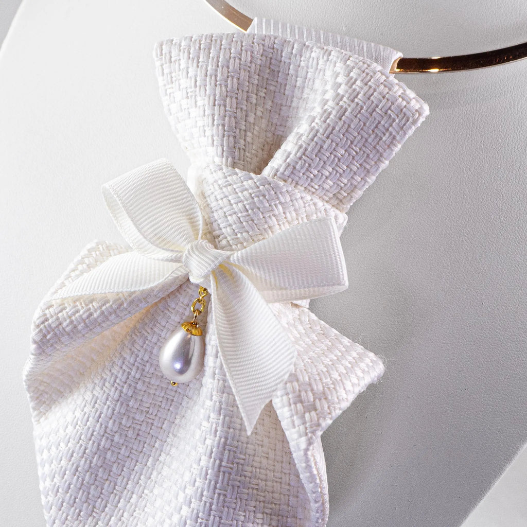 White woven fabric hair bow accessory with a large ribbon bow, pearl drop charm, and gold chain, displayed on a white mannequin bust.