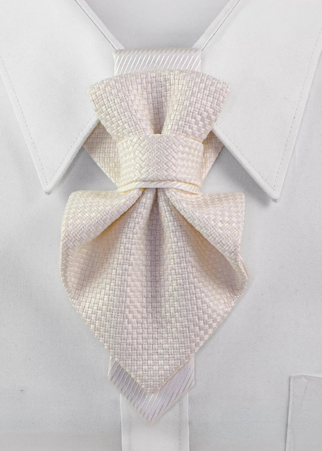 A light cream or off-white textured necktie knotted in a bow style, displayed on a white dress shirt collar Luxury handmade white Hopper Tie neck accessory for women displayed on a crisp white shirt collar. Elegant textured fabric statement tie with a minimalist satin accent, handcrafted for brides, weddings, business elegance, formal occasions, and modern fashion. Premium artisan designer neckwear showcasing timeless couture craftsmanship and sophisticated style.
