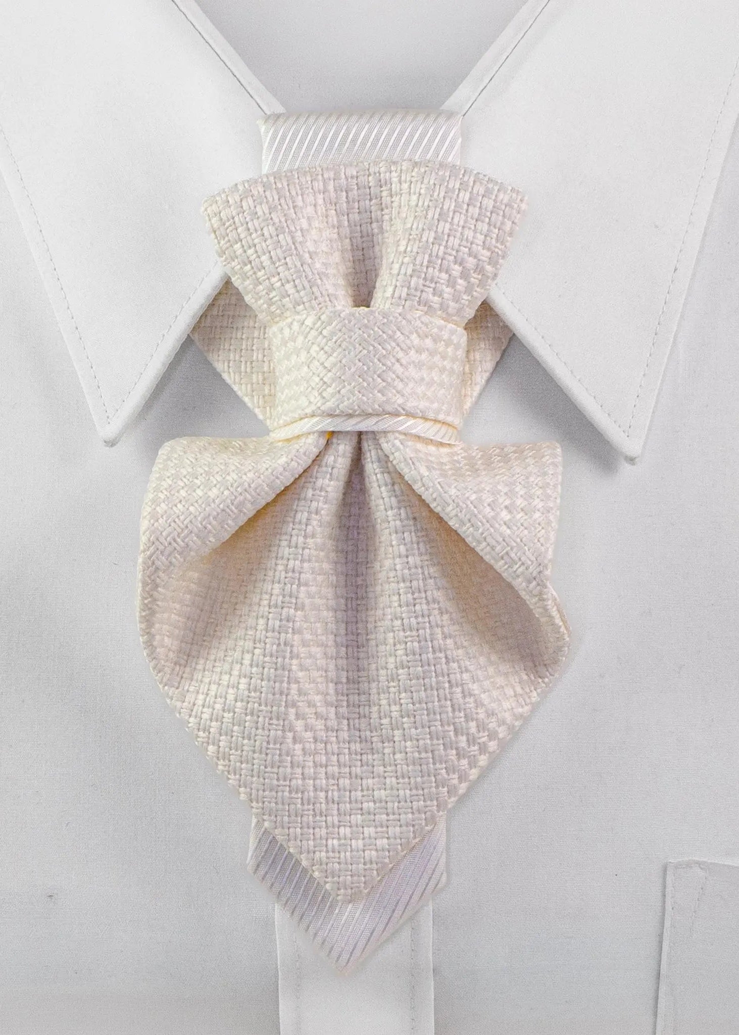 A light cream or off-white textured necktie knotted in a bow style, displayed on a white dress shirt collar Luxury handmade white Hopper Tie neck accessory for women displayed on a crisp white shirt collar. Elegant textured fabric statement tie with a minimalist satin accent, handcrafted for brides, weddings, business elegance, formal occasions, and modern fashion. Premium artisan designer neckwear showcasing timeless couture craftsmanship and sophisticated style.