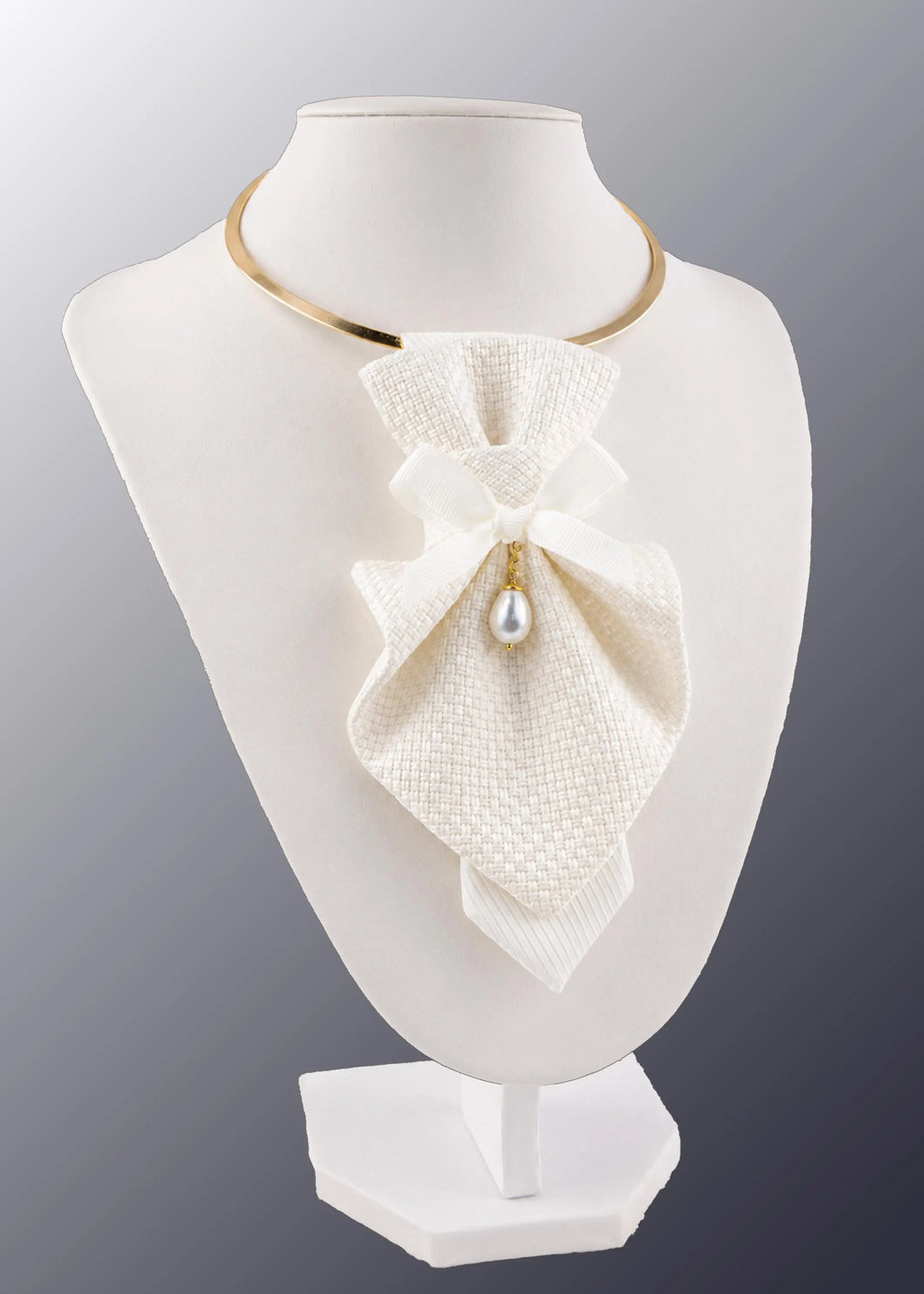 A white textured bow collar necklace with a small pearl pendant and gold chain, displayed on a white mannequin bust against a gray gradient background Luxury handmade white women's neck accessory displayed on a jewelry bust in a designer sewing studio. Elegant textured fabric choker with a satin bow, gold collar, and pearl pendant, surrounded by bridal fabrics, sewing tools, wedding dress sketches, and couture inspiration. Premium artisan statement jewellery for brides, weddings, formal events, and timeless