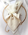 A gold-toned circular collar bar with a cream woven fabric bow, ribbon, and small pearl pendant, displayed on a white shirt collar White Hopper Tie with pearl pendant, handmade bridal neck accessory, textured white fabric tie, elegant ribbon bow, luxury wedding neckwear for women, white collared shirt, romantic bridal fashion, unique designer tie, pre-tied formal accessory, pearl necktie, wedding gift for bride, luxury handmade fashion accessory