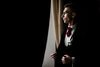 Man in a suit with a red tie standing in front of a curtain