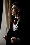 Man in a suit with a red tie standing in front of a curtain