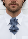 Man wearing a white shirt with a blue patterned ascot tieMan wearing a white shirt with a patterned blue bow tie against a neutral background 