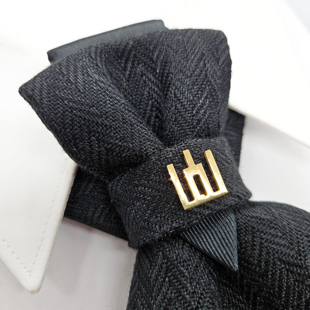 Black textured bow tie with a gold clasp on a white background