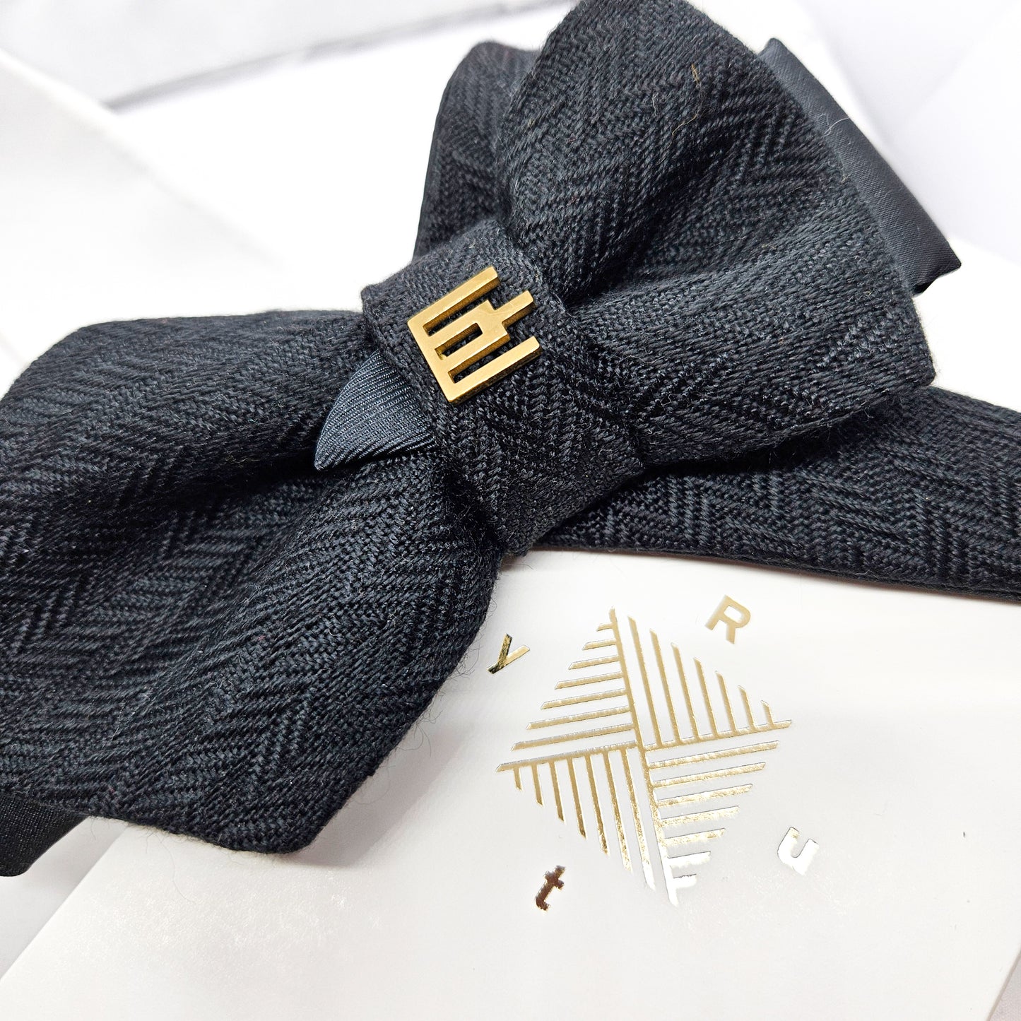 Dark gray herringbone patterned headband with a gold bow on a white background Handmade luxury dark navy blue wool bow tie with leather neck strap and unique gold-tone monogrammed clip. Pre-tied cravat for groom, weddings, formal events, and special occasions. Perfect sophisticated men's accessory.