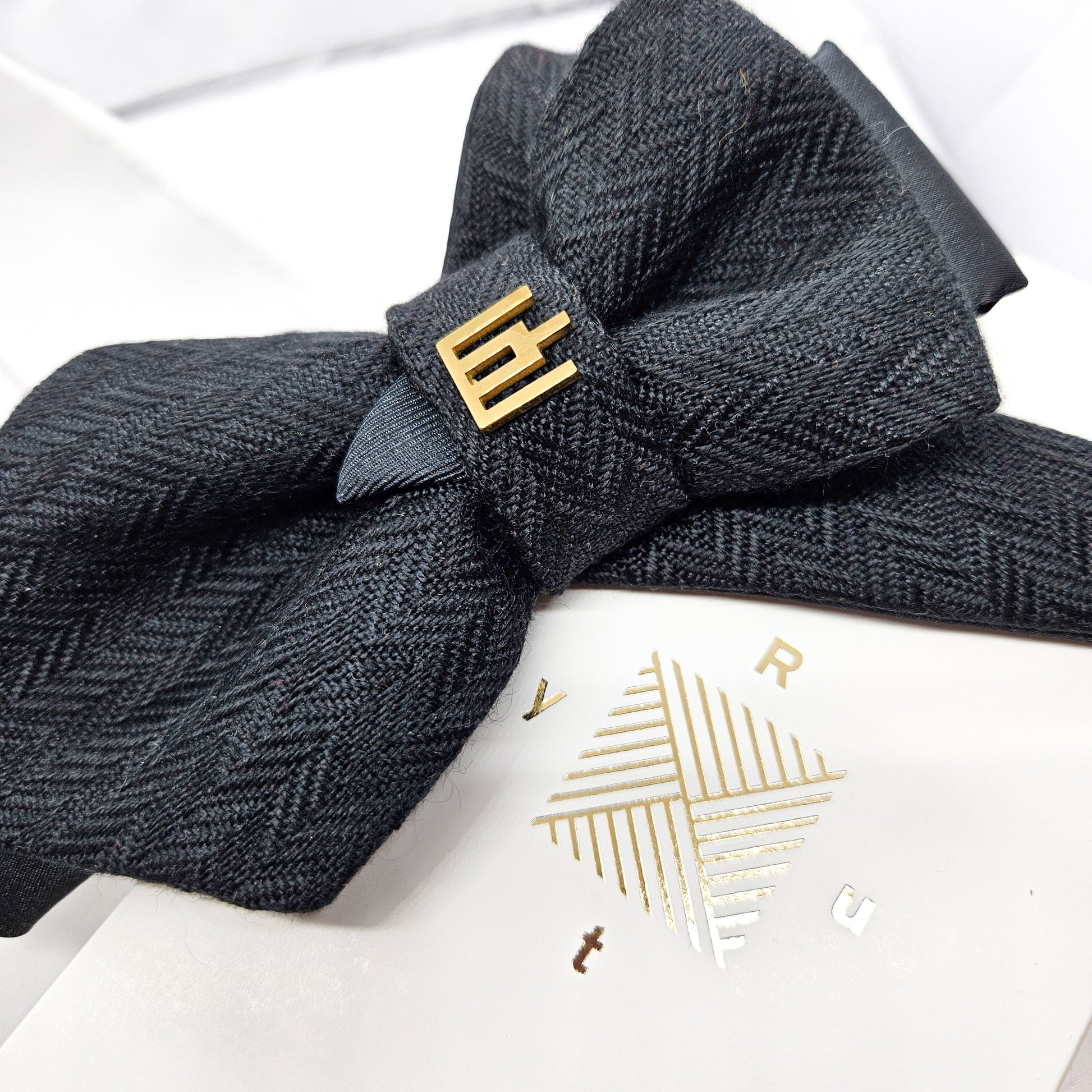 Dark gray herringbone patterned headband with a gold bow on a white background Handmade luxury dark navy blue wool bow tie with leather neck strap and unique gold-tone monogrammed clip. Pre-tied cravat for groom, weddings, formal events, and special occasions. Perfect sophisticated men's accessory.