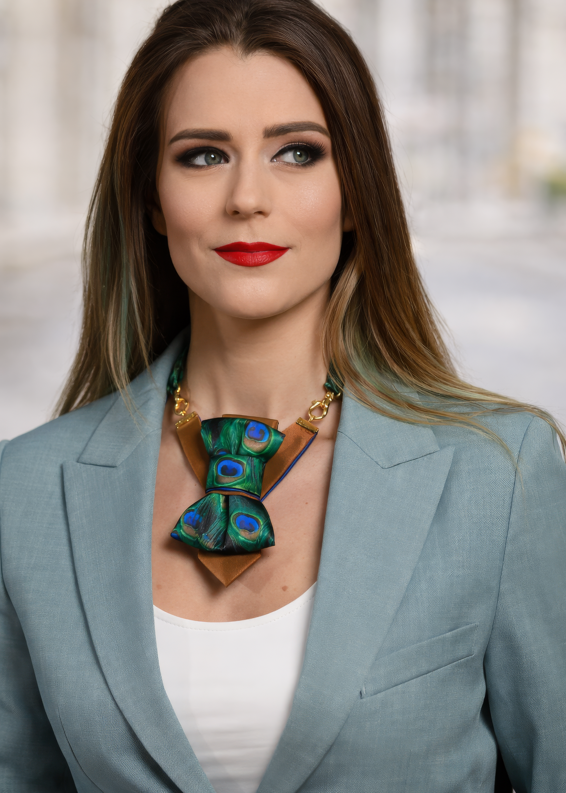 Woman wearing a stylish necklace with peacock feathers and a gray blazer peacock feather necklace, statement bow tie necklace, handmade silk accessory, green blue peacock pattern jewelry, artistic neckpiece, elegant women accessory, unique designer necklace, luxury handmade jewelry, modern bow necklace, bold statement piece, peacock motif fashion, gift for her unique jewelry, sustainable handmade accessory, artisan neckwear, teal green fashion accessory