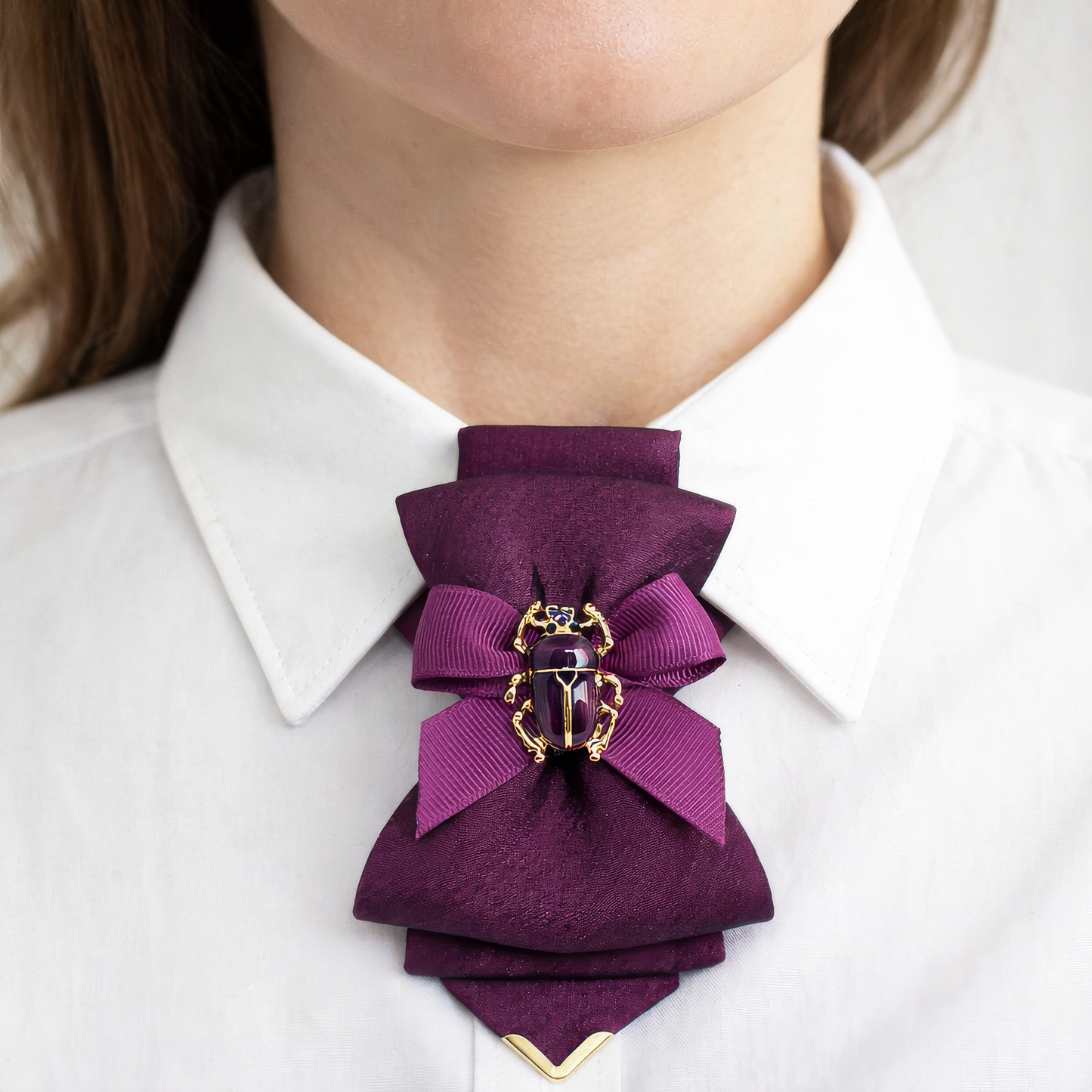 Cyclamen with Scarab woman wearing purple neck accessory close up, handmade purple women necktie, luxury female neck ornament, elegant purple bow necktie for women, artistic women neck accessory, statement neckwear for women, beetle brooch neck accessory, realistic fashion photo woman neck, natural skin tone close up, minimalist light background fashion photo
