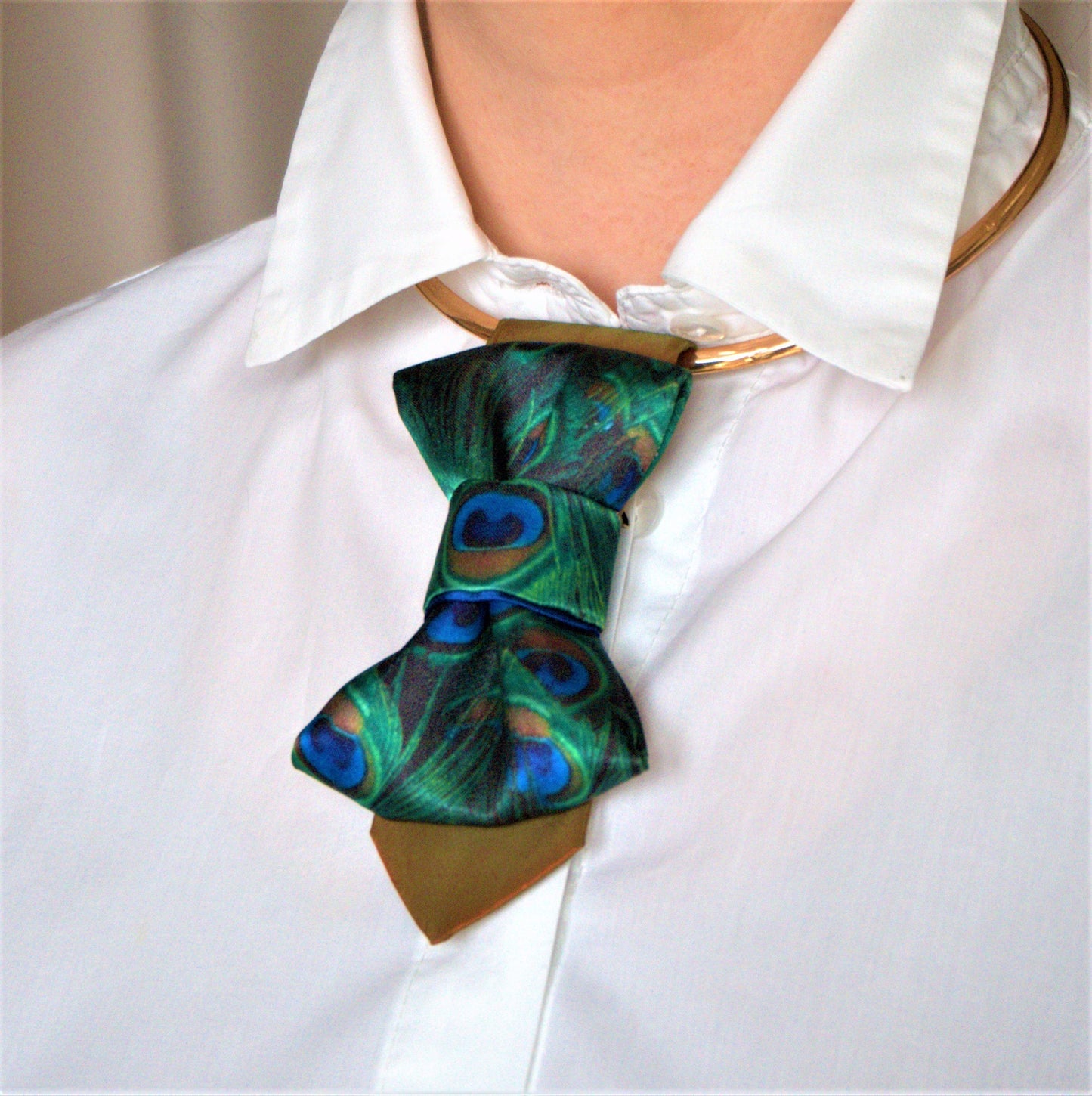BOW TIE HOPPER TIE PEACOCK Woman wearing a stylish necklace with peacock feathers and a gray blazer peacock feather necklace, statement bow tie necklace, handmade silk accessory, green blue peacock pattern jewelry, artistic neckpiece, elegant women accessory, unique designer necklace, luxury handmade jewelry, modern bow necklace, bold statement piece, peacock motif fashion, gift for her unique jewelry, sustainable handmade accessory, artisan neckwear, teal green fashion accessory