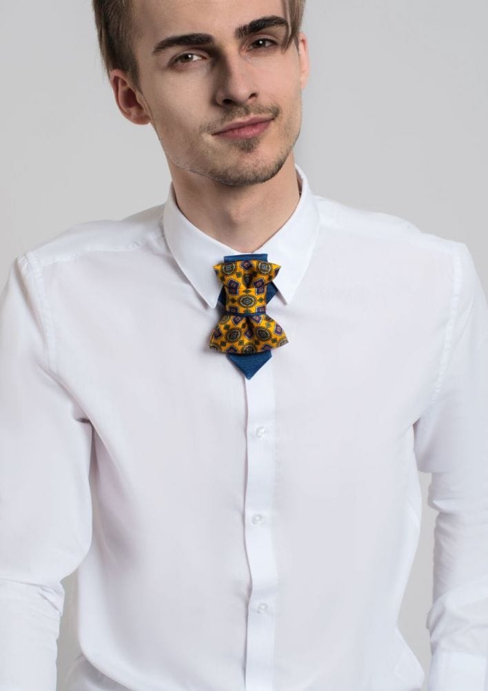 Man wearing a white shirt with a colorful bow tie against a neutral background