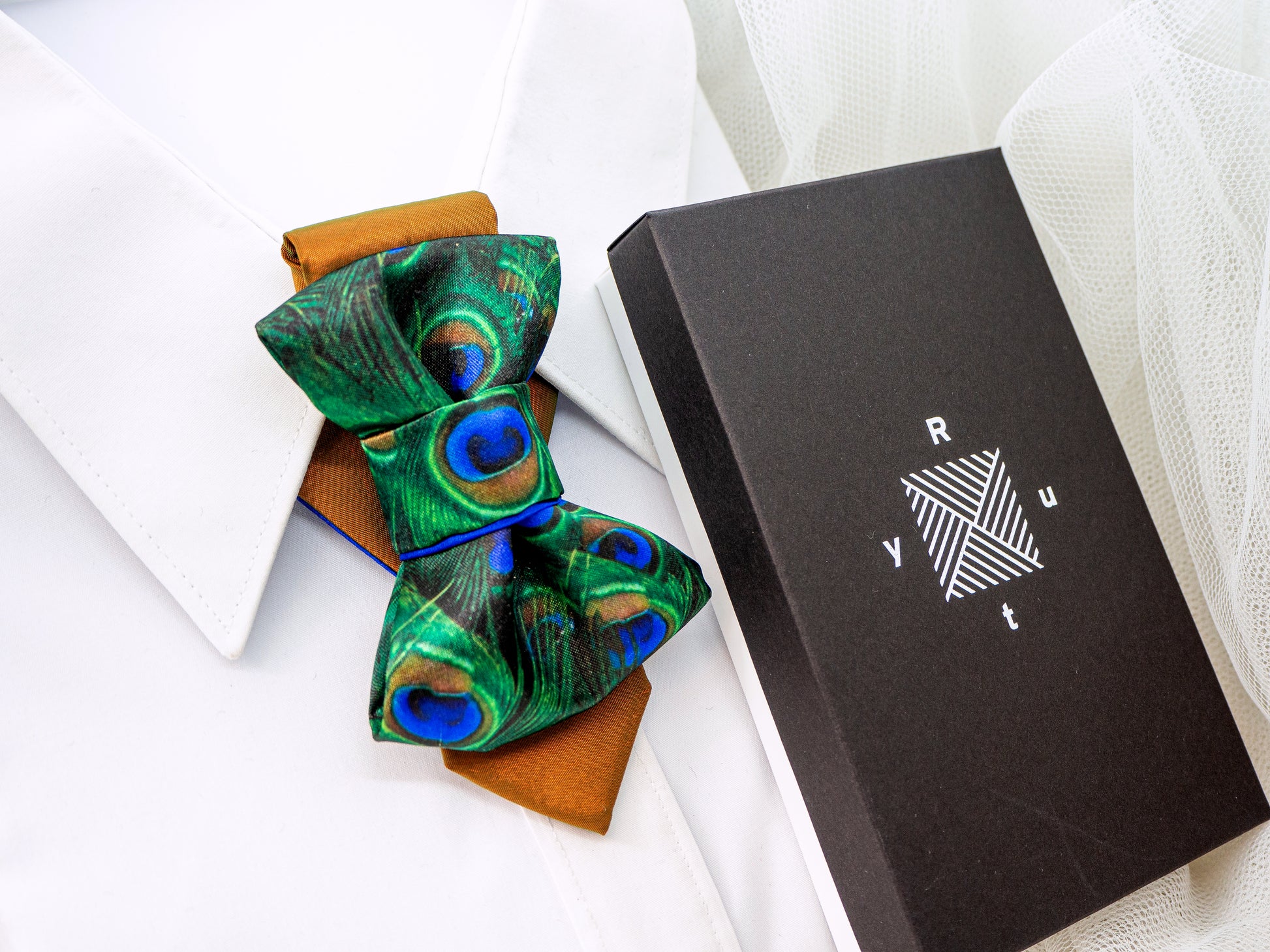 BOW TIE HOPPER TIE PEACOCK gift box Woman wearing a stylish necklace with peacock feathers and a gray blazer peacock feather necklace, statement bow tie necklace, handmade silk accessory, green blue peacock pattern jewelry, artistic neckpiece, elegant women accessory, unique designer necklace, luxury handmade jewelry, modern bow necklace, bold statement piece, peacock motif fashion, gift for her unique jewelry, sustainable handmade accessory, artisan neckwear, teal green fashion accessory