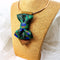 BOW TIE HOPPER TIE PEACOCK Woman wearing a stylish necklace with peacock feathers and a gray blazer peacock feather necklace, statement bow tie necklace, handmade silk accessory, green blue peacock pattern jewelry, artistic neckpiece, elegant women accessory, unique designer necklace, luxury handmade jewelry, modern bow necklace, bold statement piece, peacock motif fashion, gift for her unique jewelry, sustainable handmade accessory, artisan neckwear, teal green fashion accessory